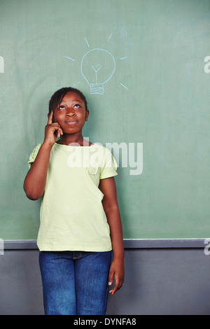 African girl having idea with lightbulb drawn on chalkboard in school Stock Photo