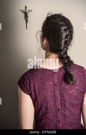 Back view of woman looking at crucifix hanging on wall Stock Photo