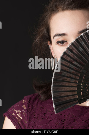 Pensive hispanic woman covering her face with foldable hand fan Stock Photo