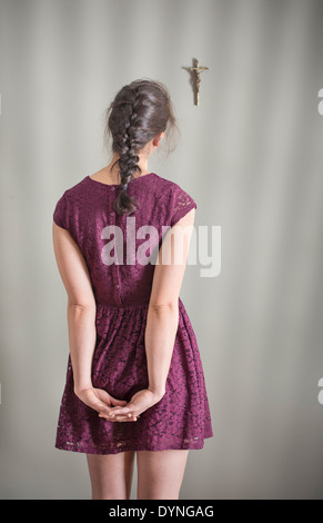 Back view of woman looking at crucifix hanging on wall Stock Photo