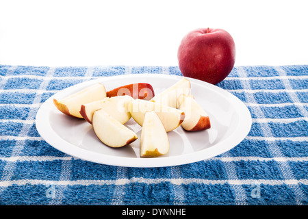 Cut up apple on a white plate on blue towel with a whole red apple against white background Stock Photo