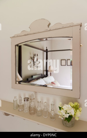 A row of vintage glass bottles on a wooden shelf below and wooden framed mirror Stock Photo