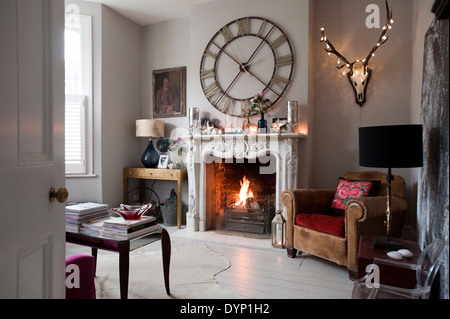 A Graham and Green 'Steeple Wall Clock' above an ornate carved marble fireplace in a living room with a vintage leather armchair Stock Photo