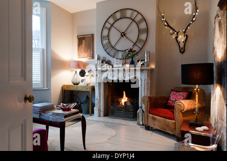 A Graham and Green 'Steeple Wall Clock' above an ornate carved marble fireplace in a living room with a vintage leather armchair Stock Photo