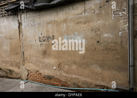 An old worn down brown wall with exposed bricks on the bottom, some Thai graffiti words written on it. Stock Photo
