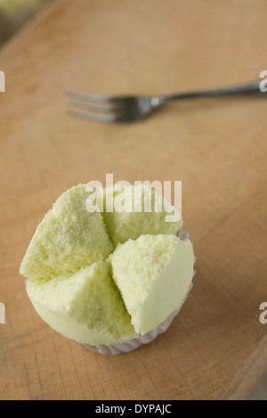 A top view shot of a beautiful light green Thai cup cake on a wooden block, a small dessert fork in the background. Stock Photo