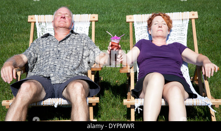 Man and woman sitting in hammocks in their backyard enjoying a tropical drink Stock Photo
