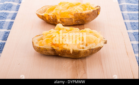 Two halves of a baked potato topped with melted cheese on a wood cutting board Stock Photo