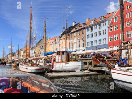 Tourists on Copenhagen canal tour boat with old wooden boats moored in front of colourful buildings on Nyhavn, Copenhagen, Zealand, Denmark Stock Photo