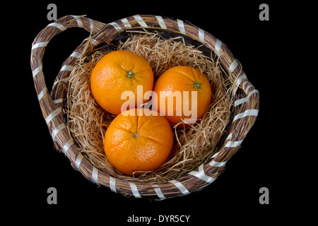 Oranges on a bed of straw in a wicker basket on a black background Stock Photo