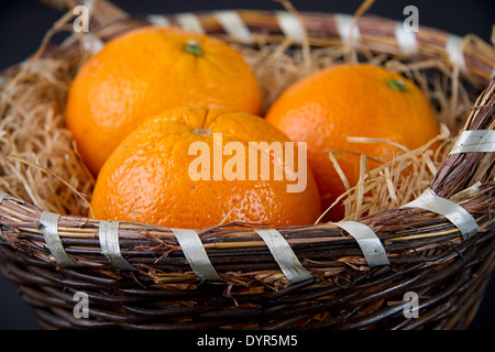 Three oranges on a bed of straw in a wicker basket against a black background Stock Photo