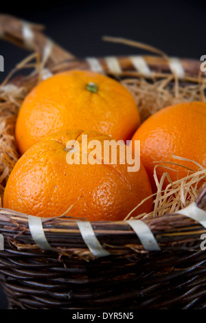 Three oranges on a bed of straw in a wicker basket against a black background Stock Photo