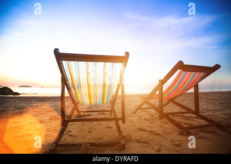 Perfect vacation concept, pair of beach loungers on the deserted coast sea at sunrise. Stock Photo