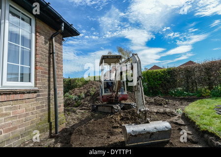 Excavating a lawn prior to laying a driveway using a micro compact excavator mechanical digger on a home improvement project. Stock Photo