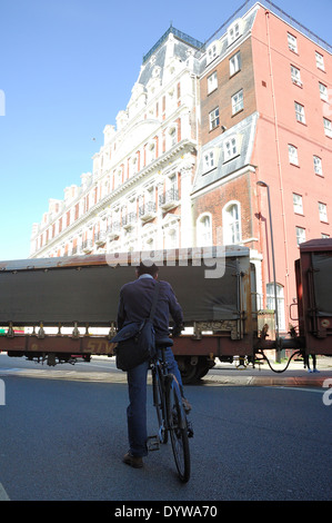 Cyclist waits on road for freight train to pass by in Southampton Stock Photo