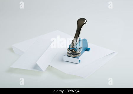 seal maker resting on a stack of white paper beside an envelope on a white table Stock Photo
