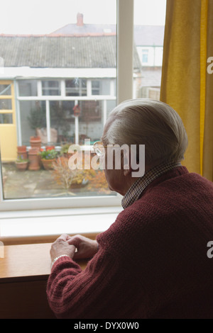 Lonely old man looking out of window at garden. Stock Photo