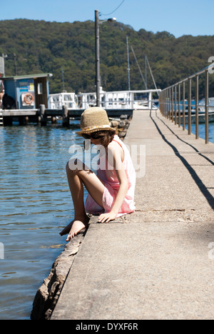 A young girl sitting on the pier leading to Tennis Court Wharf on Scotland Island, Pittwater, New South Wales, Australia Stock Photo