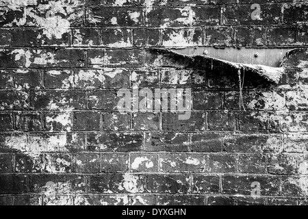 A tear in a fabric used to make a fake brick wall on a theatre set revealing the wooden background Stock Photo