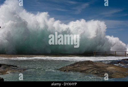 large wave crashing against rocks on the side of a ocean tidal swimming pool Stock Photo