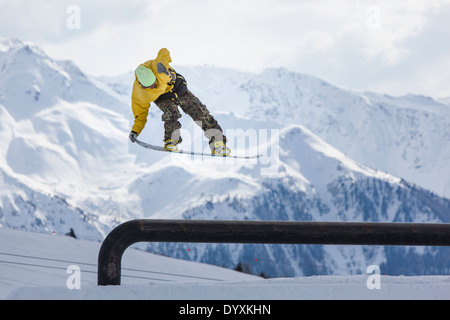 Snowboarder in woollen hat and camouflage trousers performs a tail grab aerial jump with dramatic mountains in the background. Stock Photo