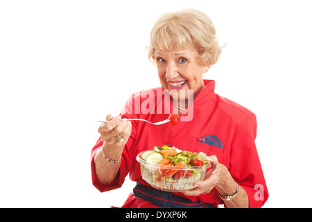 Pretty senior woman stays fit and eats healthy salad. Isolated on white. Stock Photo