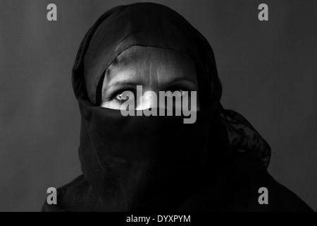 Dramatic black and white portrait of a veiled middle-aged muslim woman with strong gaze Stock Photo