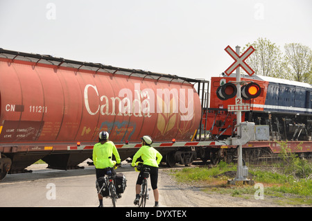 Two cyclists riding their bikes along the St Lawrence Waterway in Ontario stopped at a railway crossing. Stock Photo