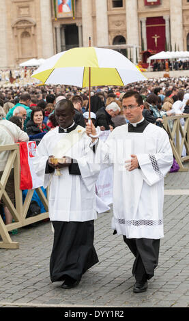 An African and a Chinese priest together going to give holy communion to the pilgrims gathered in Saint Peter's Square. Stock Photo