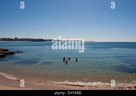 four swimmers in still aqua-blue translucent ocean water on a perfect sunny day with distant headlands Australia Stock Photo