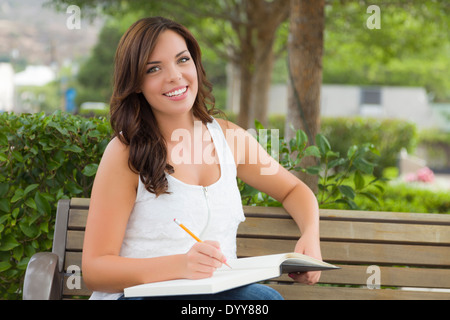 Attractive Young Adult Female Student on Bench Outdoors with Books and Pencil. Stock Photo