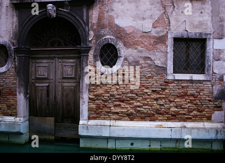Rich colour and detail of an exposed brick wall and decaying plaster on a building in a Venice canal Stock Photo