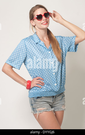 A blonde hair woman in ponytail, Caucasian female model wearing a blue polka dot top and heart sunglasses, a vintage concept Stock Photo
