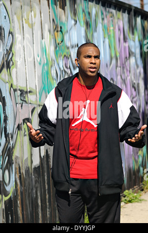 A young African American man wearing a sports jacket and t-shirt, listening to music outdoor, lifting his hands up. Stock Photo