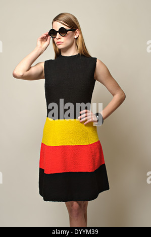 A long blonde hair woman ,Caucasian female model wearing a mod 60s black color block dress and round sunglasses posing Stock Photo