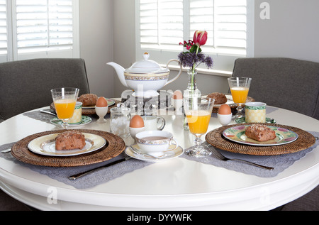 Dining table nicely laid for breakfast with sandwiches, eggs and orange juice in a brightly lit room Stock Photo