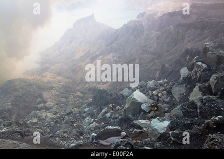 Men carrying baskets laden with blocks of sulfur from mine visible below, Kawah Ijen, Banyuwangi Regency, East Java, Indonesia Stock Photo