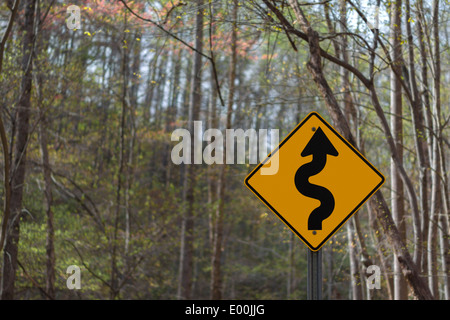 Winding road ahead yellow warning road sign in the woods Stock Photo