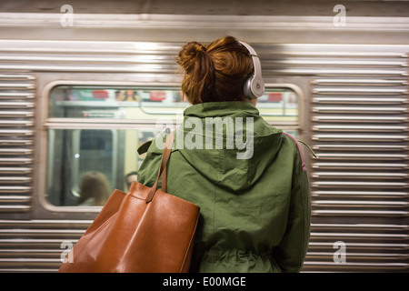 A music listener wears her Beats by Dr. Dre over the ear headphones on a subway platform in New York Stock Photo