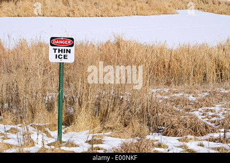 Danger thin ice warning sign near frozen pond in winter, Aurora Colorado US. Stock Photo