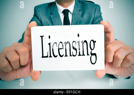 man wearing a suit sitting in a table showing a signboard with the text licensing written in it Stock Photo