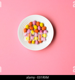 Pale pink background with white plate and multi-coloured mini eggs Stock Photo