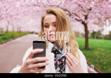 Attractive woman photographing herself at the spring garden. Beautiful young female model taking self portrait with her phone.