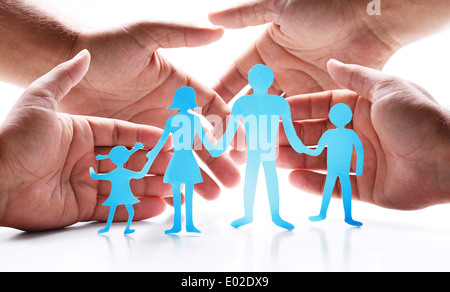 Cardboard figures of the family on a white background. The symbol of unity and happiness. Hands gently hug the family. Stock Photo