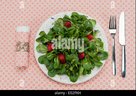 Lamb's lettuce with strawberries and flower petals served on a plate, napkin, cutlery Stock Photo