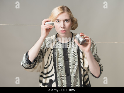 Blonde woman using tin can phone. Conceptual image of connection and communication. Stock Photo