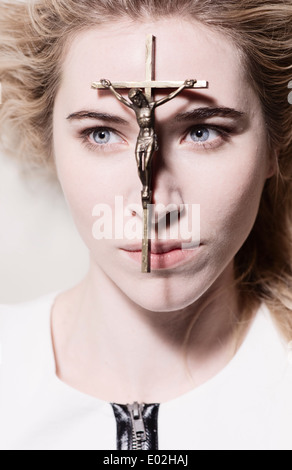 Beautiful woman with crucifix resting on her face. She is looking away with focused expression. Conceptual image of christianity, belief and hope. Stock Photo