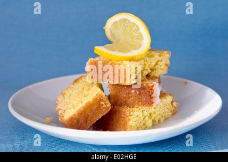 Home made lemon cake slices on plate with slice of lemon on top against blue background Stock Photo