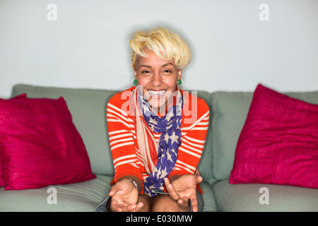 A woman with blonde hair sitting on a sofa smiling. Stock Photo