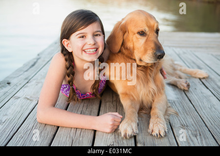 A young girl and a golden retriever dog lying on a jetty. Stock Photo